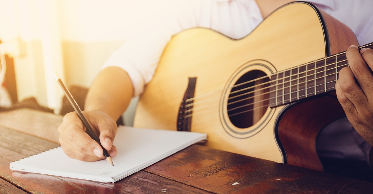 person-holding-a-guitar-while-penning-a-song